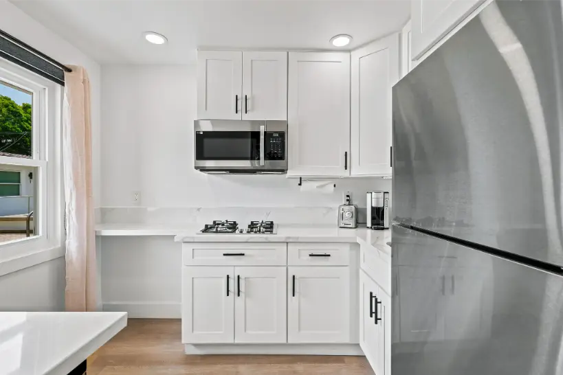 Compact white kitchen with a microwave and stainless steel refrigerator.